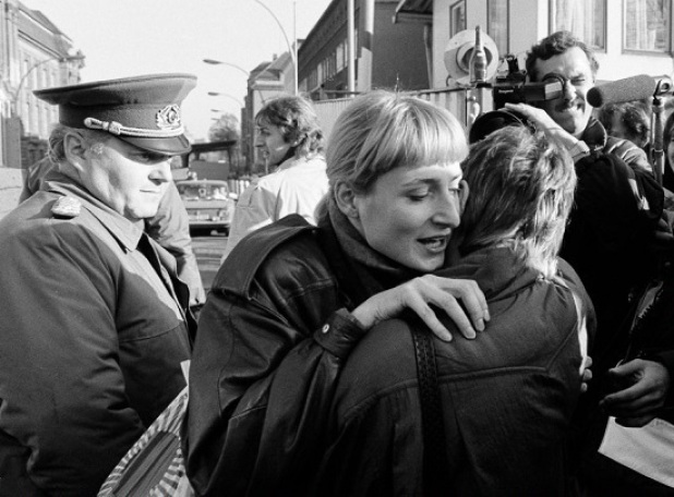 An East Berlin citizen embraces a West Berlin woman while an East German border soldier looks on in Berlin